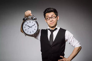 Office worker wearing a vest and a tie holding a clock up.