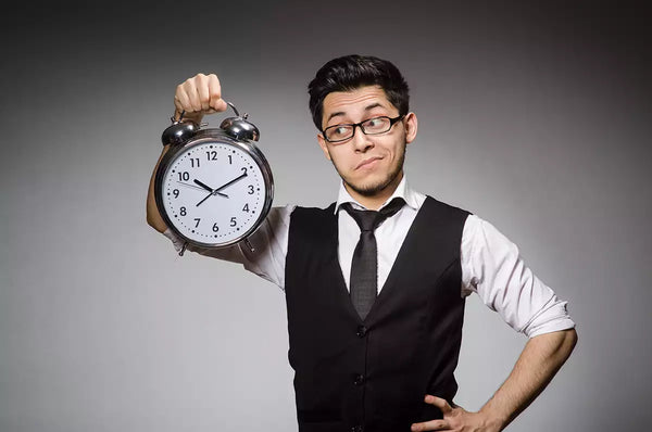 Go to article: Office worker wearing a vest and a tie holding a clock up.