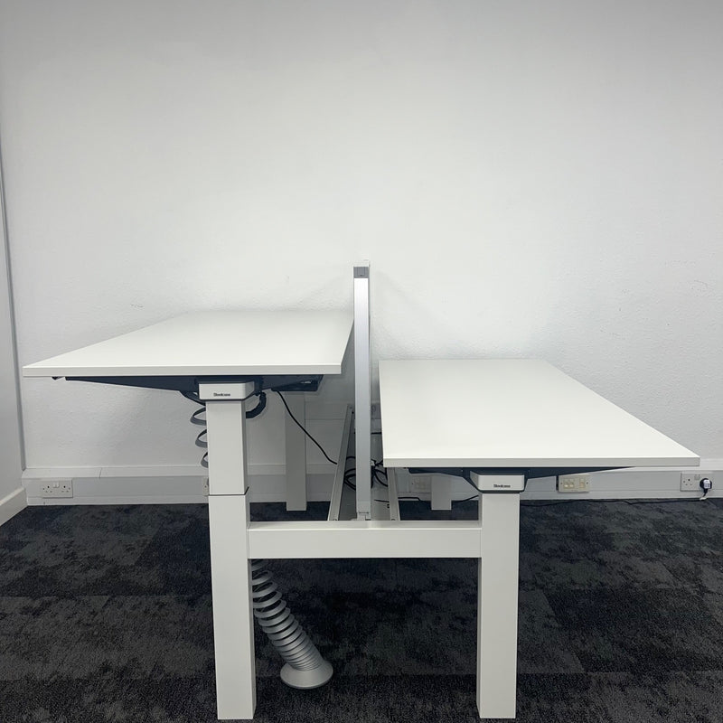 white height adjustable bench desk with two workstations. The left workstation has a raised desktop, while the right one is fully lowered, used office furniture