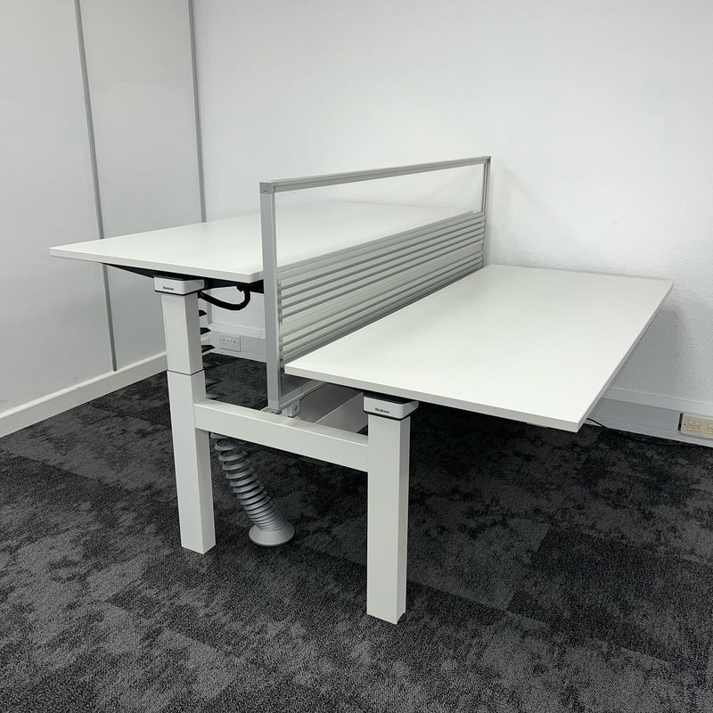Side view of a two-desk height adjustable white bench desk system with a trasparent desk divider and cable management accessories. second hand office furniture
